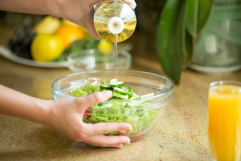 hands pouring oil green salad