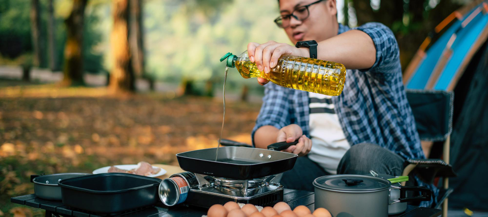 portrait asian traveler man glasses pouring sunflower oil into frying pan outdoor cooking traveling camping lifestyle concept